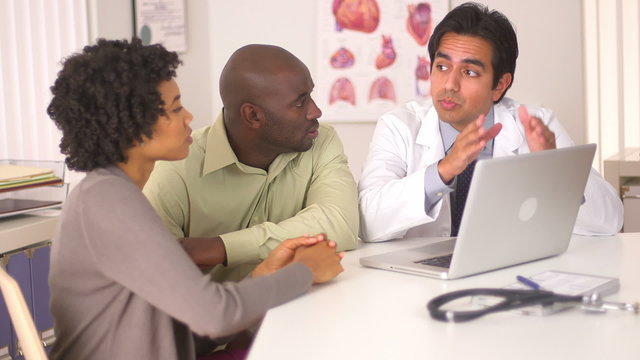 Hispanic doctor talking to African American couple with laptop c