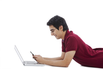 Man lying in front of a laptop and using a mobile phone