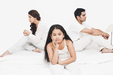 Girl sitting with her parents on the bed looking serious