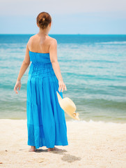 Woman in blue dress throws hat on the beach