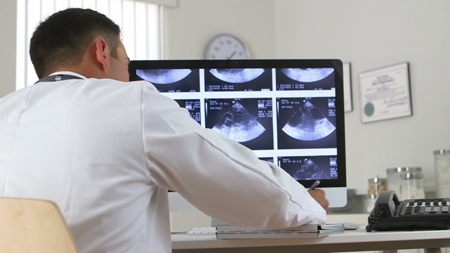 Latino doctor viewing sonogram on computer while talking on phon