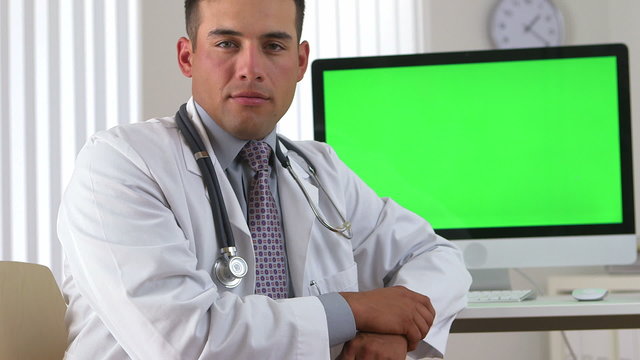 Hispanic doctor sitting with green screen on computer in backgro