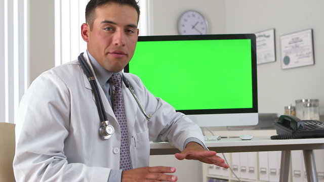 Hispanic doctor looking back to greenscreen on computer in backg