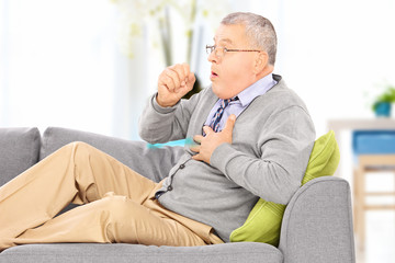 Fototapeta premium Mature man seated on a sofa coughing at home