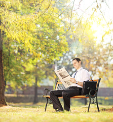 Fototapeta premium Young man on bench working on a laptop in a park