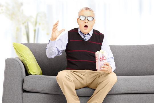 Shocked senior man with popcorn sitting on sofa and watching