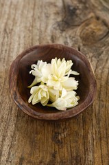 White flower petals in bowl on old wood background
