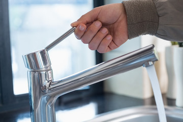 Plumber's hand opening a water tap at bathroom