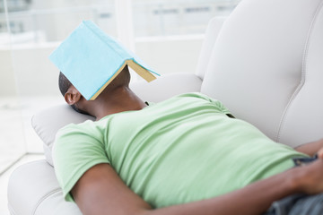 Fototapeta premium Relaxed man with book over face lying on sofa