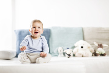 Adorable laughing baby boy sitting on sofa and looking up.