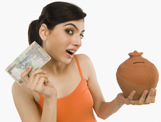 Woman holding Indian currency notes with a piggy bank