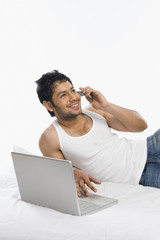 Man talking on a mobile phone with a laptop and smiling