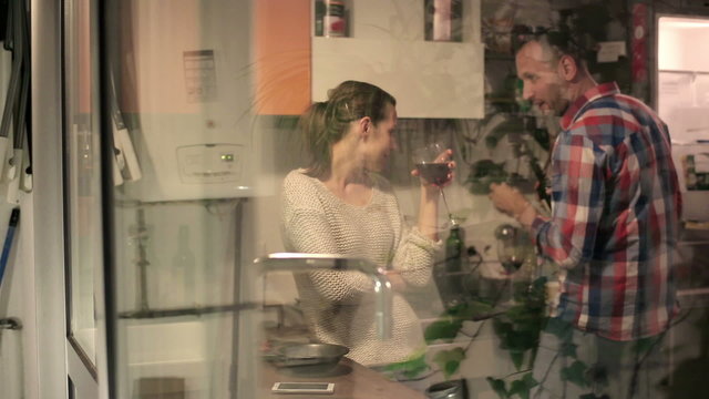 Happy couple talking and drinking wine in kitchen at home