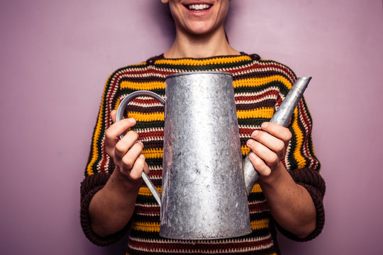 Happy young woman holding metal watering can