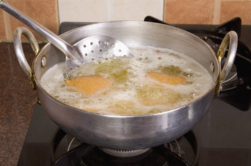 Close-up of pakoras being fried in a pan on a stove
