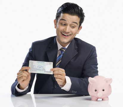 Businessman holding a currency note and looking at a piggy bank