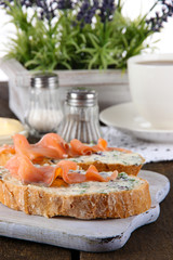 Fish sandwiches and cup of tea on cutting board on wooden table