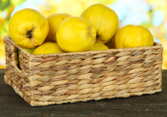 Sweet quinces in wicker basket on table on bright background