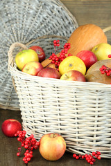 Juicy apples and pumpkin in wooden basket on table close-up