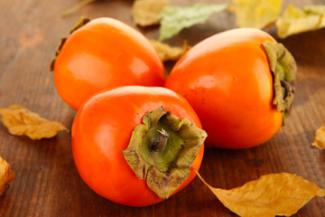 Ripe persimmons with yellow leaves on wooden background