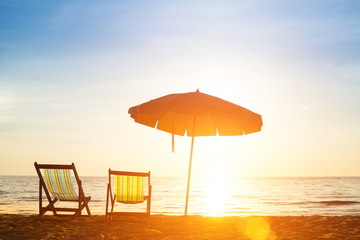 Pair of beach loungers on the deserted coast sea at sunrise.