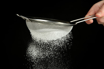 Sieve and powdered sugar on black background