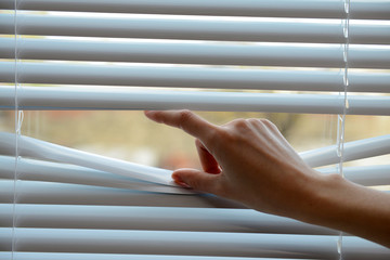 Female hand separating slats of venetian blinds with a finger