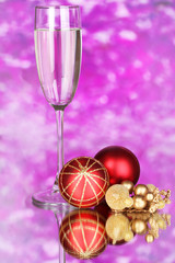 Glass of champagne and Christmas balls on purple background