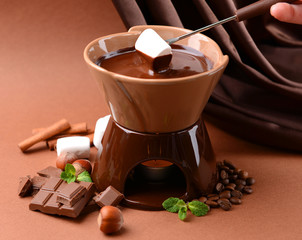 Chocolate fondue with marshmallow candies, on brown background