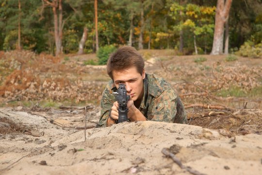 Teenager, boy lying in his battle dress and a rifle
