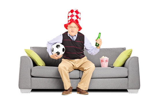 Mature sport fan holding a ball and beer watching sport