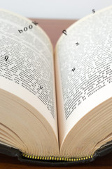 Fototapeta premium Old open book with magic falling letters on wood