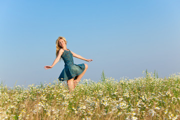 The happy young woman jumps in the field  of camomiles..