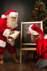 Santa Claus with his helper standing near chalkboard with wishli