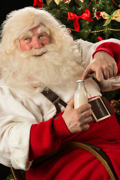 Happy Santa Claus opening glass bottle with milk against Christm
