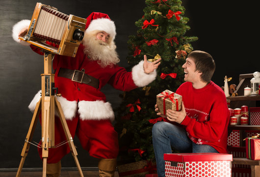 Santa Claus taking picture of cheerful man with old wooden camer