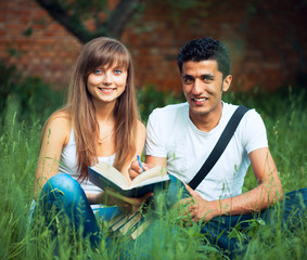 Two students guy and girl studying in park on grass with book