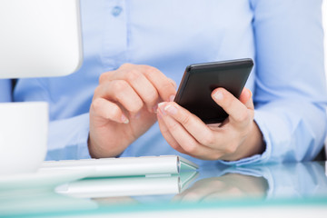 Businesswoman Using Cellphone Sitting In Front Of Computer
