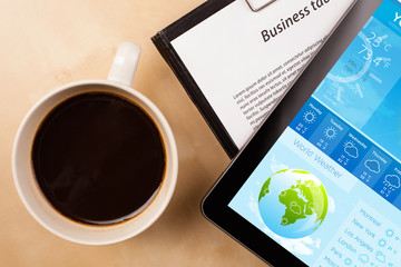 Tablet pc showing weather forecast on screen with a cup of coffe