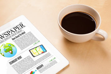 Tablet pc shows news on screen with a cup of coffee on a desk