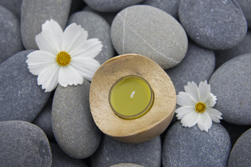 Fototapeta na wymiar candle and two white flower on gray pebbles