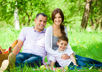 Happy family of three has picnic in green park