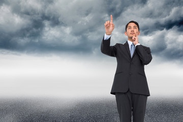 Composite image of thoughtful asian businessman pointing