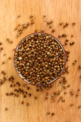 Heap coriander seeds in bowl on wooden background close-up