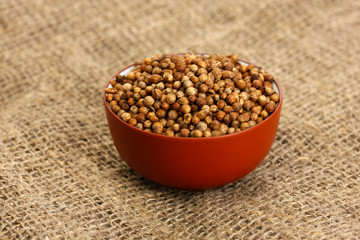 Heap coriander seeds in bowl on canvas background close-up