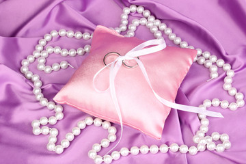 Wedding rings on satin pillow on purple cloth background