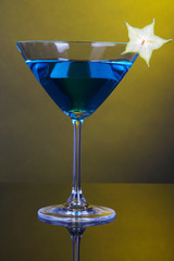 Blue cocktail in martini glass on dark yellow background
