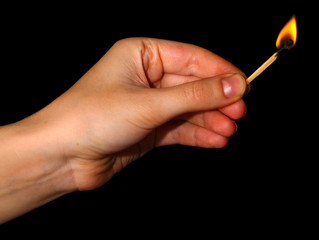 Burning match in hand on black background