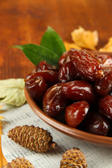Dried dates on plate with yellow leaves on wooden background