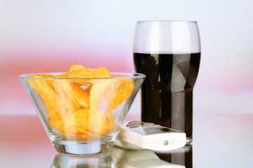 Chips in bowl, cola and TV remote on bright background